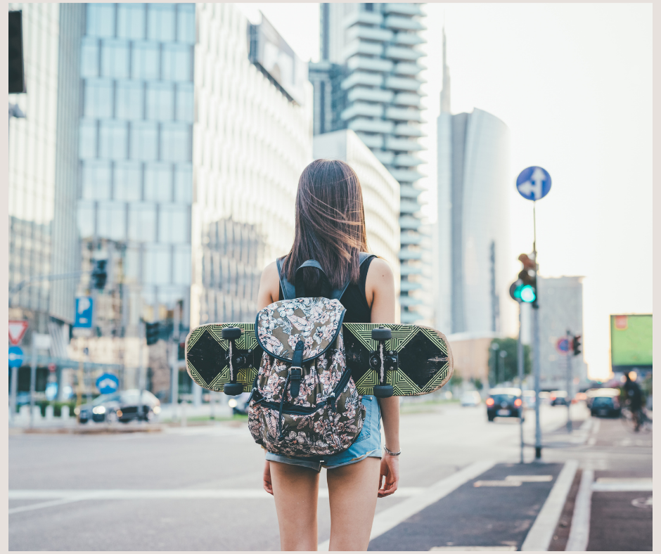 Young female with skateboard and backpack preparing to enter a crosswalk